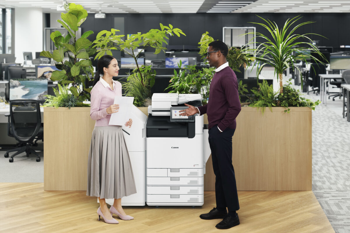 Two coworkers talking beside a Canon imageFORCE multifunction printer in a modern open plan office